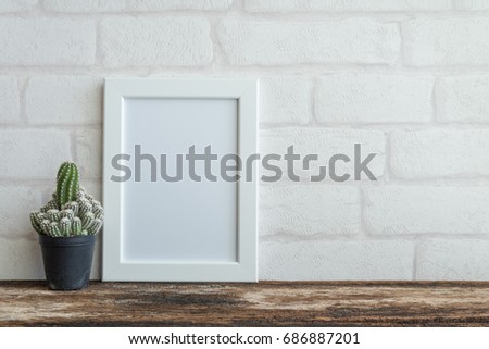 Photo frame on old wooden table with cactus over white brick wallpaper background