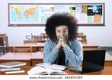 Picture of an Afro college student looks depressed while learning with a laptop and textbooks on the desk