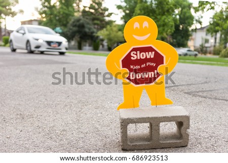 Slow down kids at play sign on busy residential street with car passing