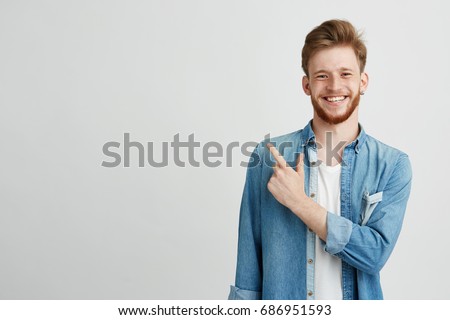 Portrait of cheerful young man smiling looking at camera pointing finger up over white background. Royalty-Free Stock Photo #686951593