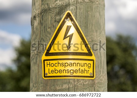 German high voltage sign mounted on wooden pole with green trees in background