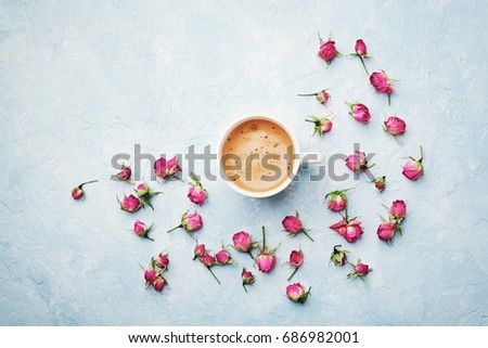 Morning coffee cup and dry rose flowers on blue vintage table top view in flat lay style. Cozy breakfast on Mother or Woman day.