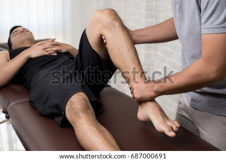 Therapist treating injured leg of athlete male patient in clinic - sport physical therapy concept Royalty-Free Stock Photo #687000691