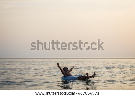 Man with a raised hands smile and enjoy summer on rubber ring in the sea water