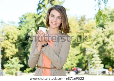 Young beautiful woman is drinking coffee or hot tea on the nature background.