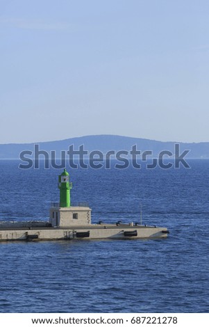 Lighthouse on commercial dock for ships and boats, Photo of green lighthouse on harbor with blue sea in the background