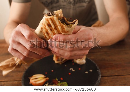 Man eating shawarma on big plate. Grilled lavash with meat and herbs, close up picture. Customer in restaurant