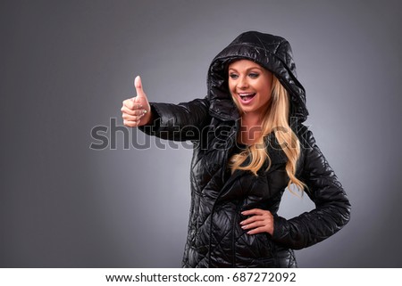 A beautiful young woman standing in a winter jacket and showing thumbs up
