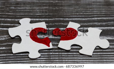 Two puzzles with a painted heart on the background of a wooden table. Heart connection, love.