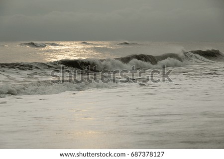 A long powerful brown wave run to the coastline, weather is stormy, sky is low and grey, picture is dramatic. 