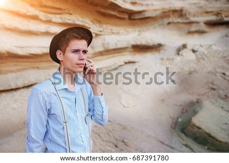 Attractive man is standing in the middle of a sand quarry and making a call from a smartphone.