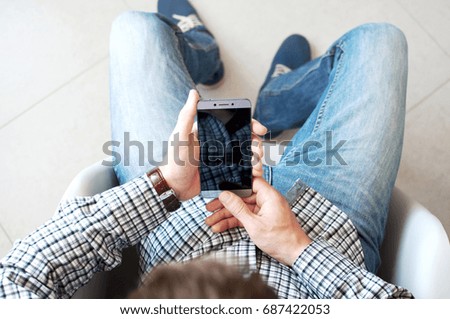 Top view of the hand of a young man in a checkered shirt using a smartphone. Touch screen phone business.