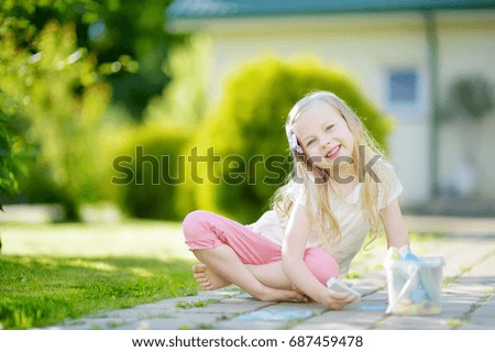Cute little girl drawing with colorful chalks on a sidewalk. Summer activity for small kids. Creative leisure for family.