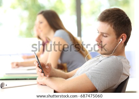 Bad student distracted listening to music sitting in a classroom