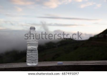 A water bottle rests on a wooden board. Fog and mountain backdrop
