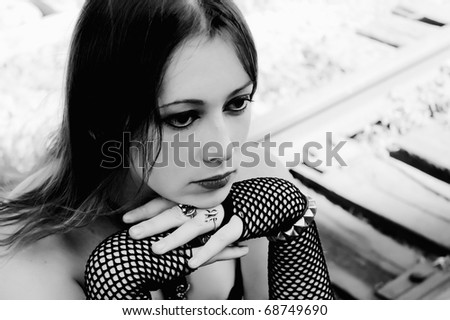 Closeup portrait of sad gothic girl sitting on rails. Black and white photo