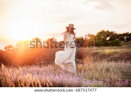 The beautiful girl in the dress is having fun on the hill at sunset. The girl is walking down the hill at sunset