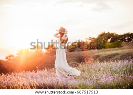 The beautiful girl in the dress is having fun on the hill at sunset. Girl in a hat, dancing at sunset. The girl is walking down the hill at sunset