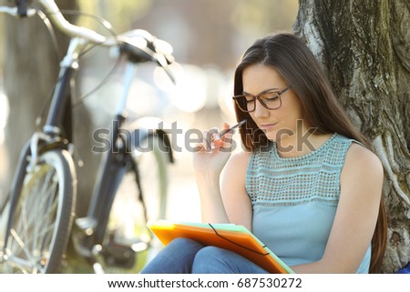 Single student wearing eyeglasses memorizing notes sitting in a park Royalty-Free Stock Photo #687530272