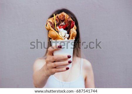 Young woman holding bubble waffle with fruits, chocolate and marshmallow, selective focus.