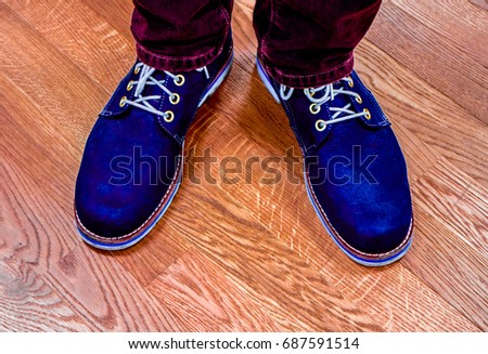 dark blue big lather boots with golden circles and shoelace against wooden floor. Boots and burgundy jeans against floor. Close up view on man's legs