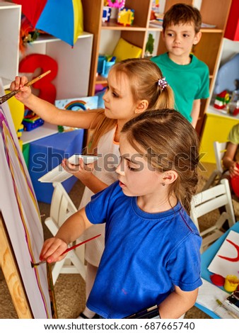 Children painting finger on easel. Group of kids girl and boy with teacher learn paint in class school. Child picture on background. Students draw a rainbow. Preparation for an art exhibition.