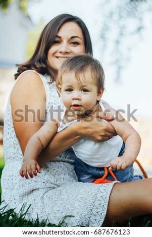 Portrait of happy little mom kissing and shake baby outdoors on green summer garden with fresh green grass background Cute mother embracing baby looking at camera.