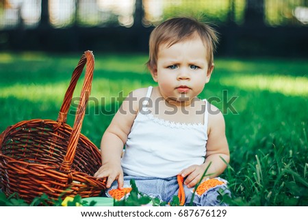 baby is seriously looking into the camera. She frowns. Sitting on grass. outdoor