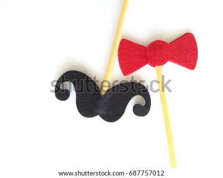 Top or flat lay view of Photo booth props red bow tie and a black mustache on a white background flat lay. Birthday parties and weddings.

