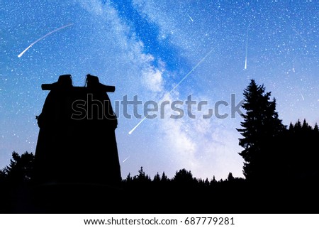 A view of the stars of the Milky Way with a silhouette of a pine trees forest and an astronomical observatory in the mountain. Falling stars during the summer when it is best for astro observations.