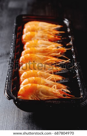 Fresh raw shrimps in a bowl on a wooden table. Eating seafood. Dark background