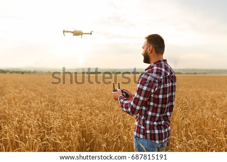 Farmer holds remote controller with his hands while copter is flying on background. Drone hovers behind the pilot in wheat field. No face. Agricultural new technologies and innovations concept