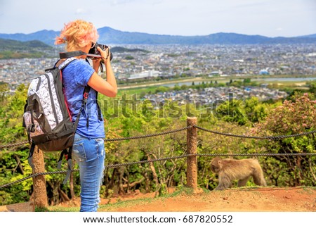 Nature woman photographer with camera takes picture of Kyoto skyline. Caucasian female with backpack shooting of Japanese macaque. Professional photographer in Iwatayama Monkey Park, Arashiyama, Japan