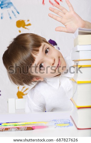 Schoolboy of 7 years old dressed in a shirt,sitting at the table with a pile of dictionaries