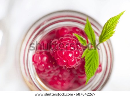 Raspberries in glass jar with leaves. Flat lay, top view.