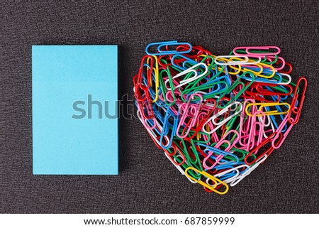 Variety of color paper clips arranged in heart shape on black background.