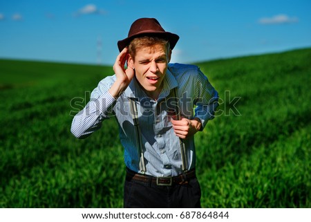 Handsome man in the nature tries to hear something with putting his hand to his ears.