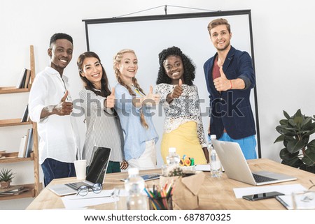 portrait of multiethnic smiling business people showing thumbs up in office