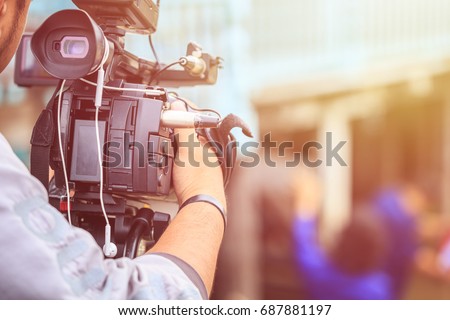 Cameraman using black professional digital video camera. Outdoor setup and working Royalty-Free Stock Photo #687881197