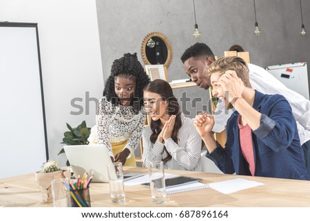 multicultural excited business people looking at laptop screen together at workplace in office