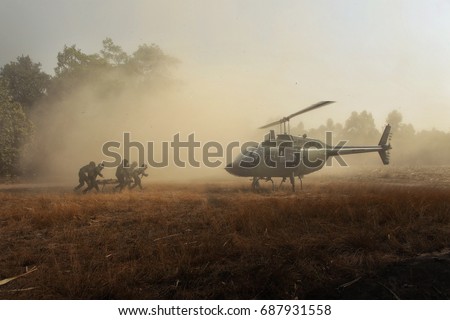 Sending injured soldiers back by helicopter. Group of elite unit combat soldiers carrying a wounded friend on a stretcher through a sandy terrain after a fierce battle against terrorists.
