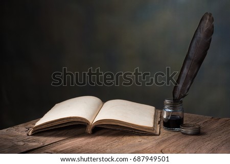 still life photography : feather pen with inkwell and opening old book on old wooden table against art dark background