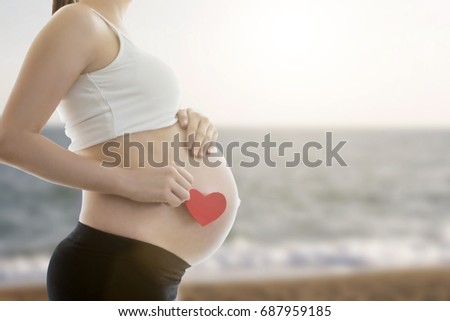Pregnant's woman belly with heart on the beach 