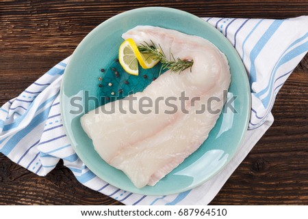 Fresh halibut fillet with lemon and rosemary on plate on wooden table from above. Fresh seafood fish eating.