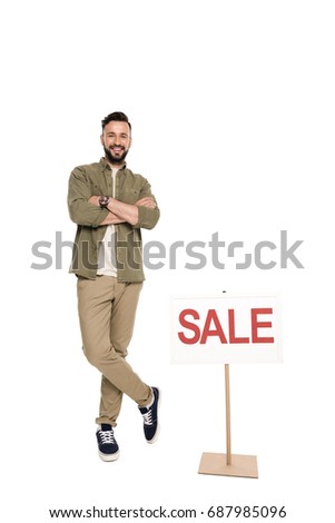 smiling man with arms crossed standing near sale sign isolated on white