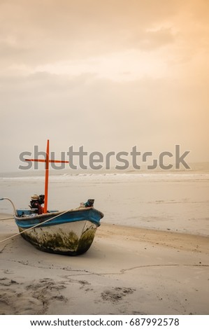 Old fishing boat stay parking on the white sand with beautiful sunset at Hua Hin beach, Thailand. Sea on golden sky background. (warm mood) (Selective focus)