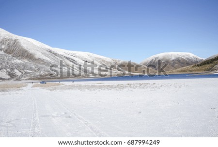A white field covered by snow with a Beautiful Lake near snow mountains at South Island, New Zealand.