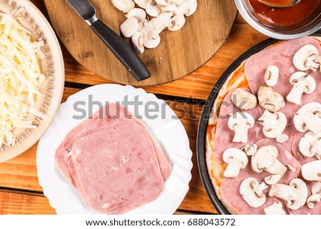 Table with ingredients for preparing pizza. Sliced mushrooms ham bowl with ketchup.