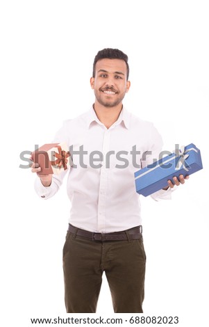 Handsome young man smiling and holding gift boxes, guy wearing white shirt and brown trousers, isolated on white background
