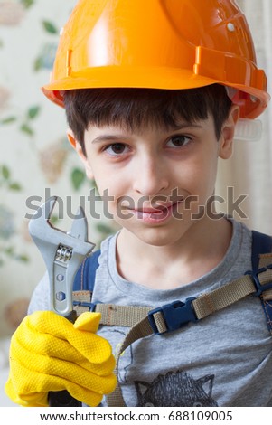 Boy in a protective helmet and with a wrench in the image of a builder